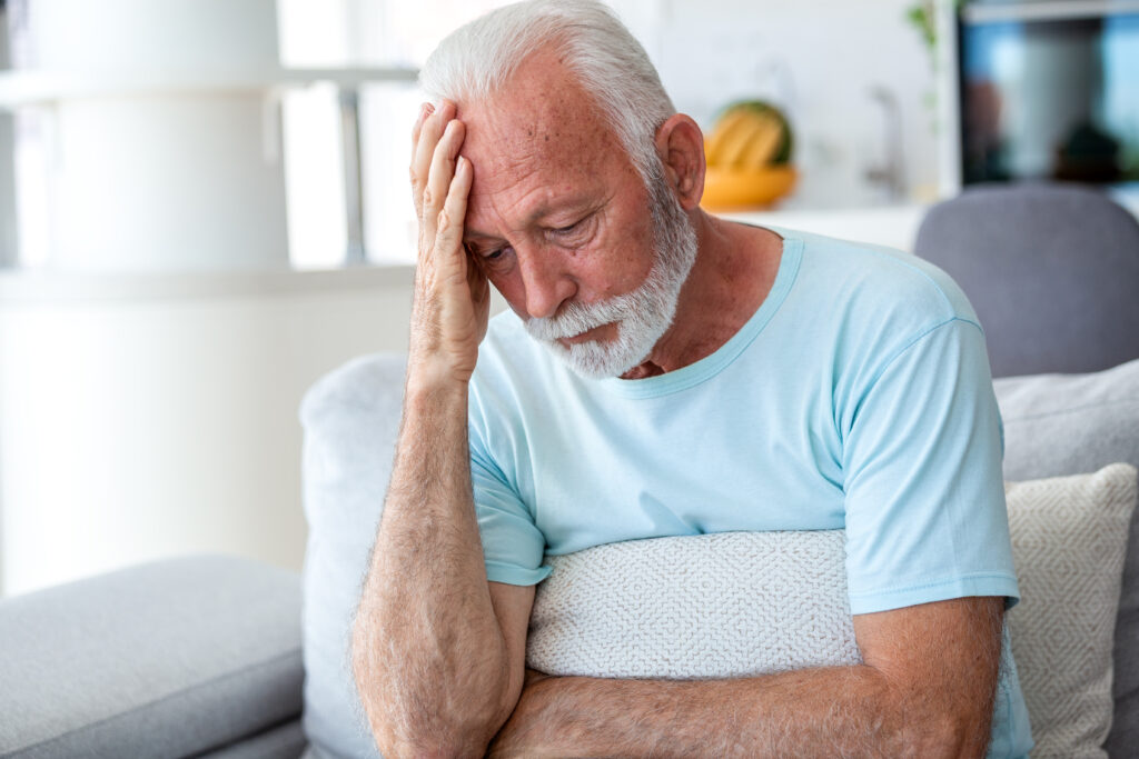 Headache and migraine. Sad senior man sitting with hand on forehead, people with stress and mental health problem, healthcare and medicine concept. Tired retired male feeling unwell on sofa.
